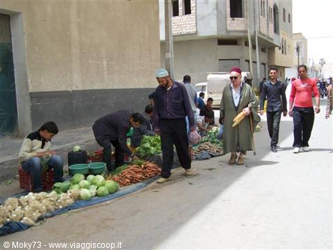 Street vegetable market: cabbages and carrots on the ground, people strolling by