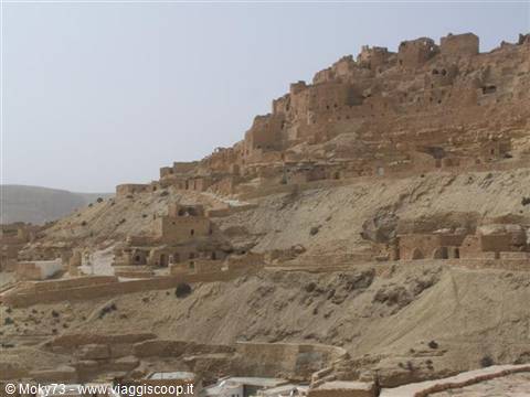 Berber mud-brick village built on the rocky hillside under hazy sky