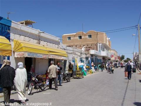 Market street with men in djellabas, scooters and stalls under yellow awnings