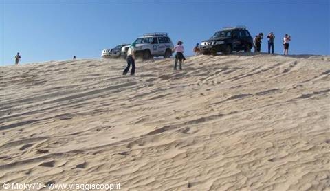 Tourists and off-road vehicles on a sand dune ridge under blue sky