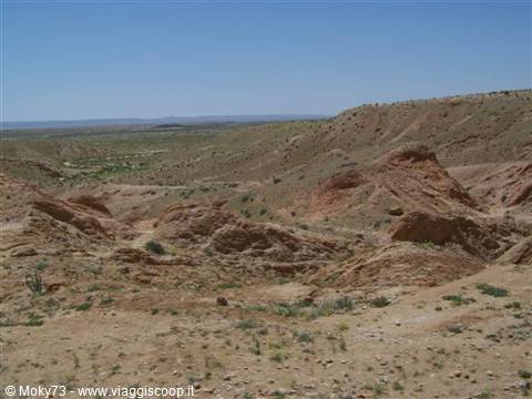 Eroded rocky desert hills under blue sky with sparse vegetation