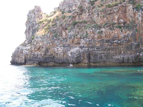 Boat near limestone cliffs on clear turquoise water