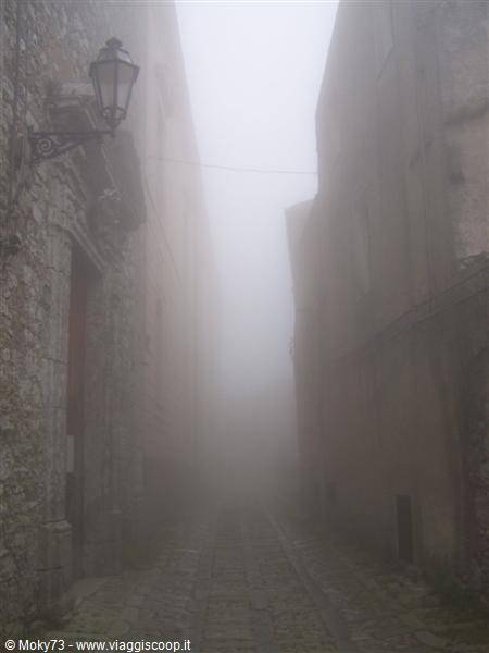Foggy cobblestone alley between old stone walls, antique lantern