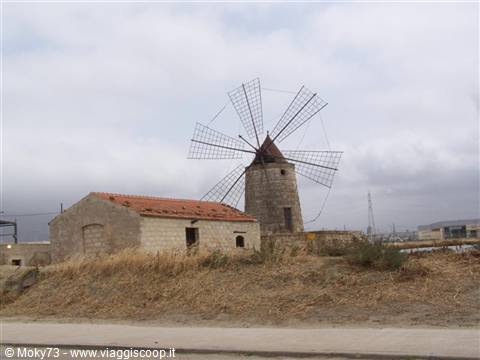 Stone windmill with wooden sails beside a small brick house