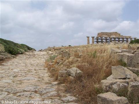 Ancient stone-paved road through ruins and dry grass toward Selinunte's Doric temple