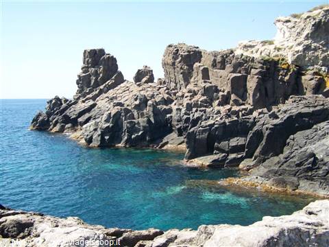 Black lava cliffs plunge into turquoise water under bright sunlight