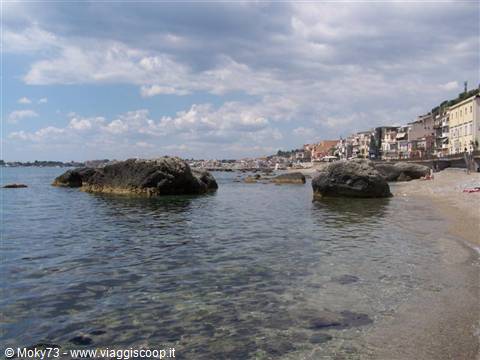 Black rocks in clear water in front of colorful beachfront houses