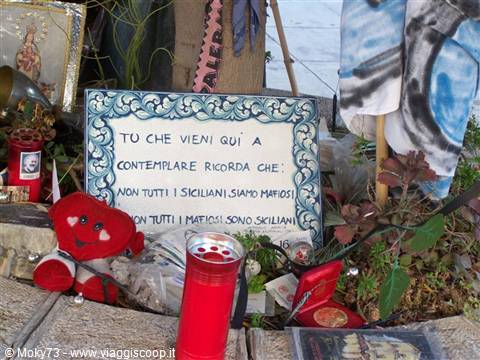 Roadside shrine with painted sign, lit red candle, plush heart and plants