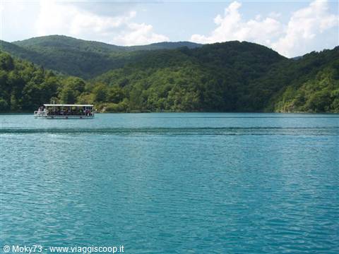 Tourist ferry crossing the turquoise Plitvice lake among forested green hills