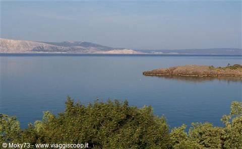 calm blue sea with a rocky islet and green trees in the foreground
