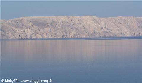 Limestone cliffs reflected on calm sea under blue sky