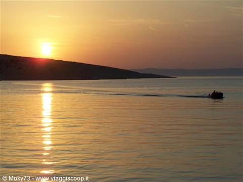 Lone motorboat crosses the golden sea before a dark hill