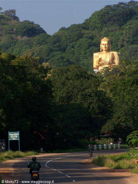 Cyclists on a country road below the giant golden Buddha of Dambulla