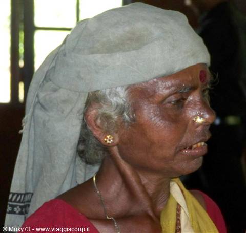 Elderly woman in grey headwrap with red bindi and gold earring inside temple
