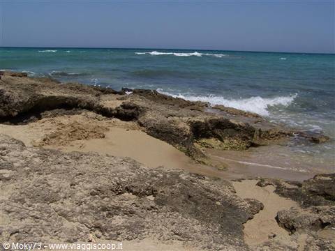 Limestone rocks and sand on the shore, waves breaking into the turquoise sea