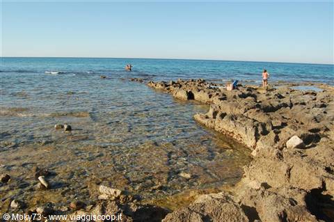 Rocky shoreline with clear shallow water, people swimming and standing