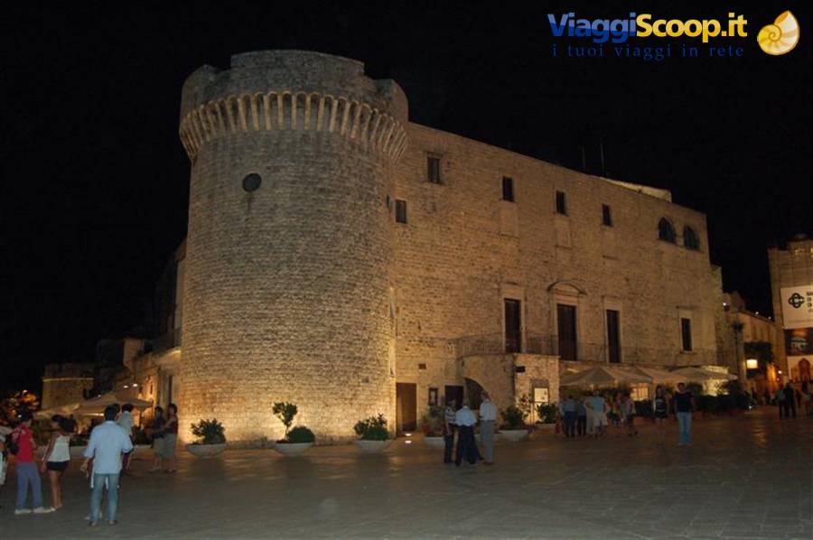 Conversano castle at night, illuminated round stone tower, people strolling in the square