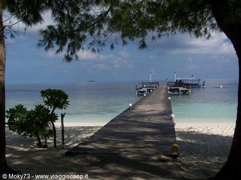 Wooden jetty over white sand leading to dock with anchored boat