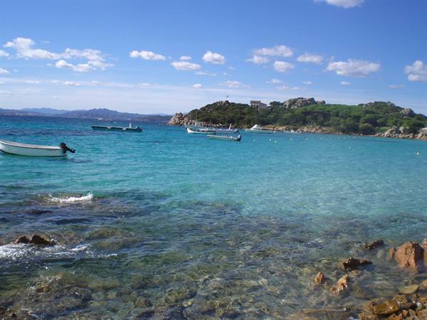 White boat and pink rocks in turquoise water, green island with houses behind