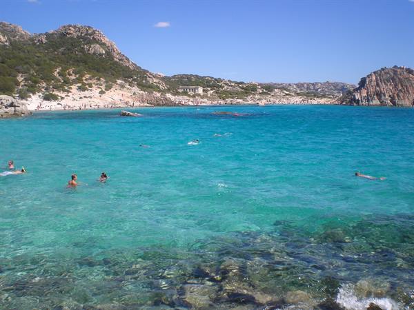 Swimmers in clear turquoise water among granite rocks and hills, Sardinia