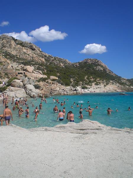 Swimmers in turquoise water among granite rocks and Mediterranean scrub, Caprera beach