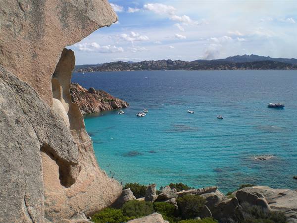 Pink granite rocks over turquoise water with boats, islands in the distance