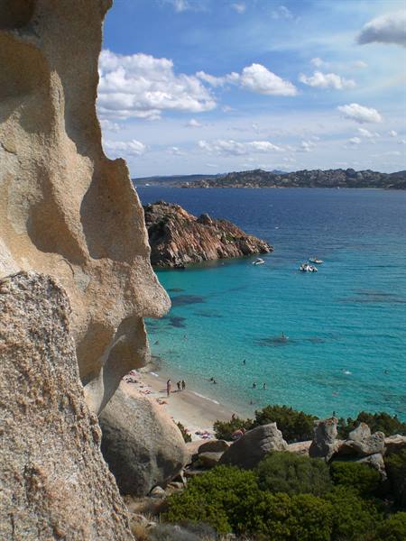 Wind-sculpted granite rocks frame a turquoise cove with anchored boats and swimmers