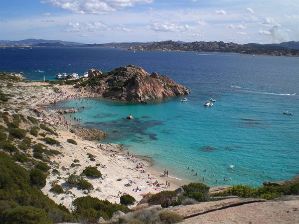 Granite beach and turquoise water with swimmers and boats, La Maddalena