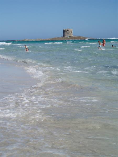 Swimmers in turquoise waves in front of the Aragonese tower at La Pelosa