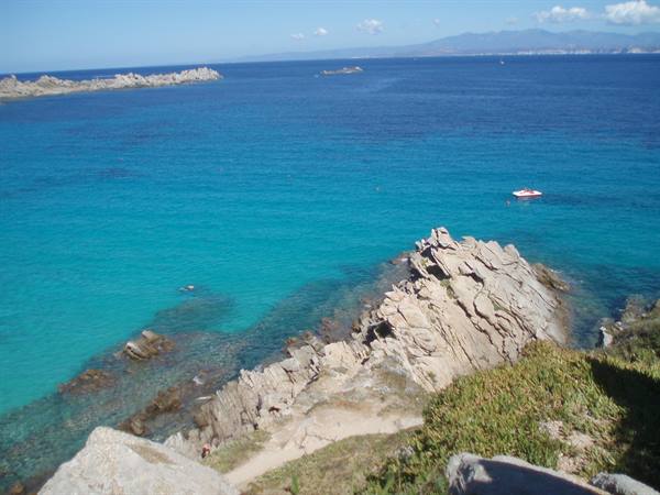Granite rocks over turquoise sea, motorboat offshore, green vegetation in foreground