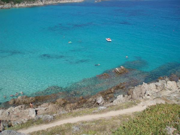 Boat and swimmers in turquoise water, path over granite rocks