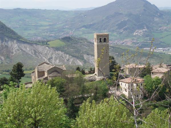 Stone tower and church above San Leo village, green rolling hills
