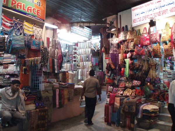 Covered souk with stalls of colorful bags and fabrics, man walking through
