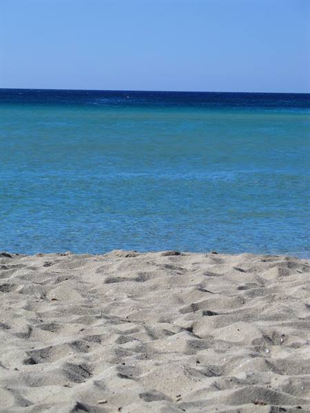 Pale rippled sand in front of turquoise sea and clear blue sky