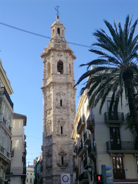 Valencia's baroque stone tower beside buildings and palm trees in daylight