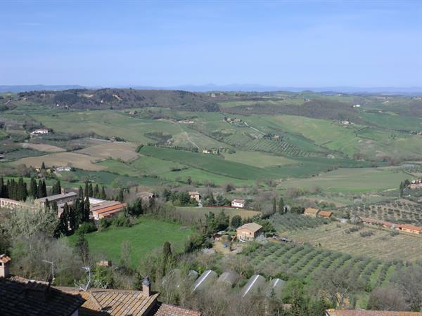 Cultivated hills with farmhouses and greenhouses under a blue sky