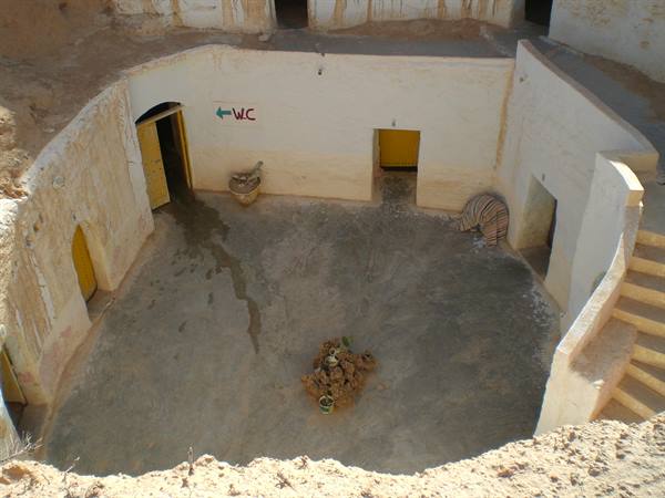 Sunken troglodyte courtyard in Matmata, yellow doors, staircase and WC sign