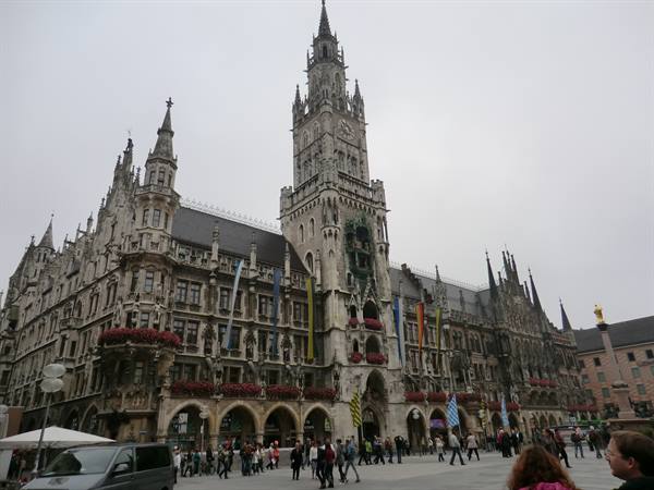 Munich's Gothic New Town Hall tower, tourists crossing the square under grey sky
