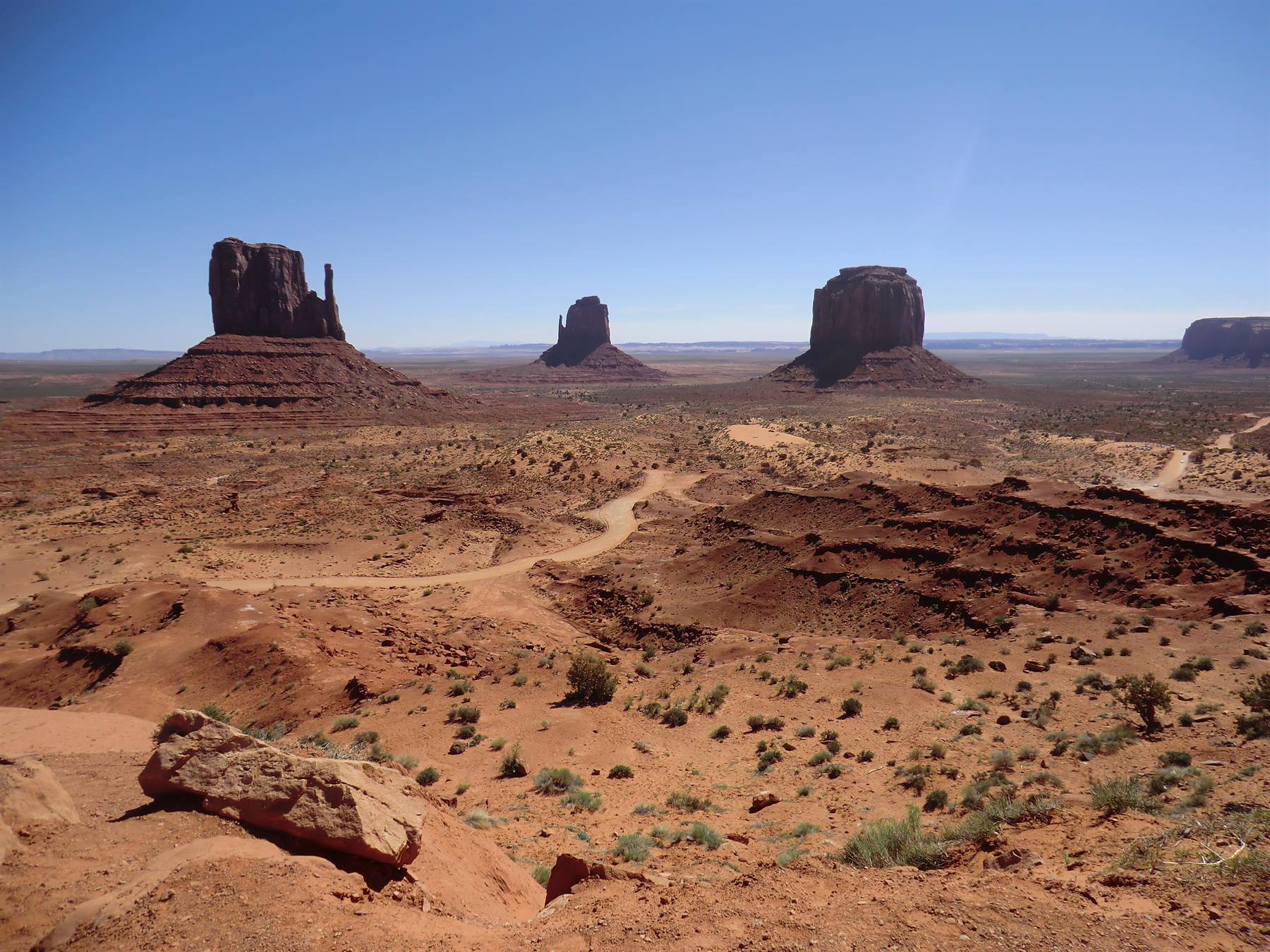 Monument Valley: butte rosse di arenaria sopra sabbia e arbusti, cielo azzurro