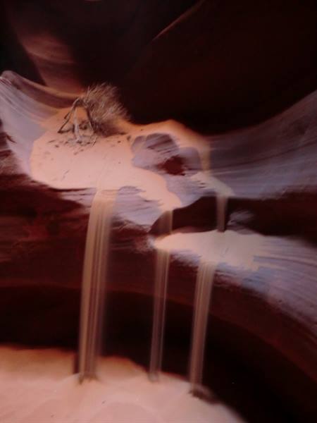 Sand cascading over wavy red rock inside Antelope Canyon