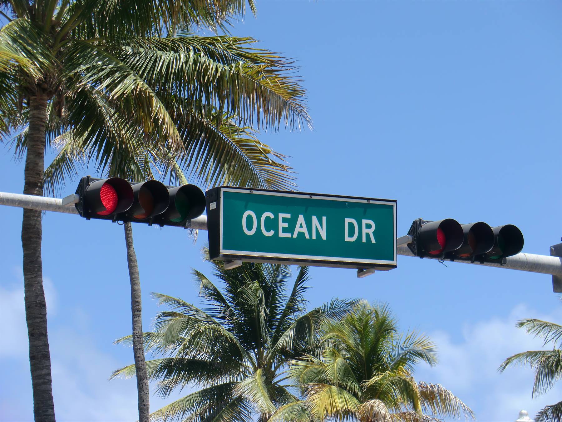 Cartello verde di Ocean Drive tra semafori rossi e palme contro cielo azzurro