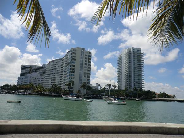 Boats anchored in green water, white towers and palms under clouds