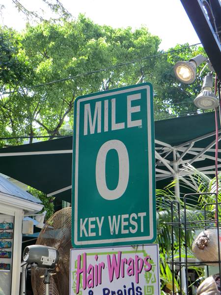 Green Mile 0 sign in Key West among awnings, fans and trees