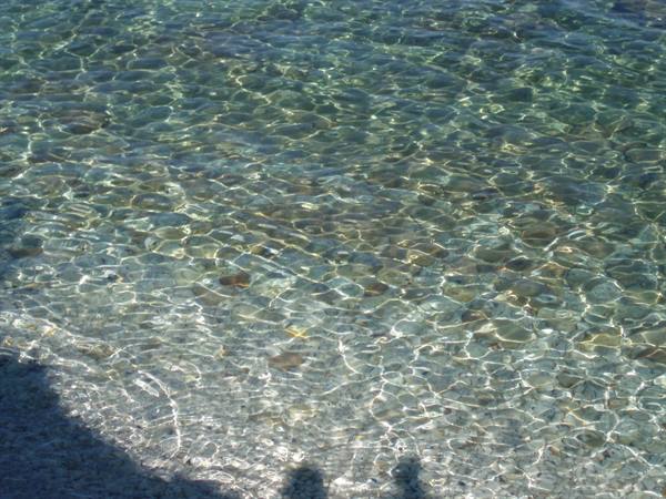 Crystal-clear shallow water shimmering over pebbles under sunlight