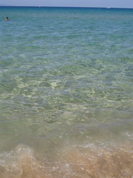 Clear turquoise water over pale sand, one swimmer far offshore