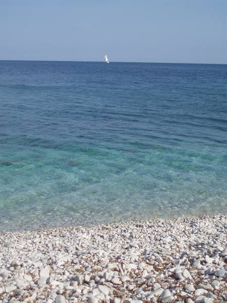 White pebble beach, clear turquoise water, a sailboat on the horizon