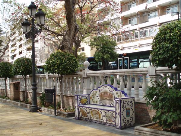 Ceramic-tiled bench in blue and white, wrought-iron lampposts and city bus behind