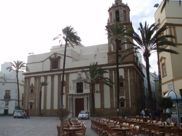 Cadiz Cathedral with stone bell tower, palm trees and bar tables in the square