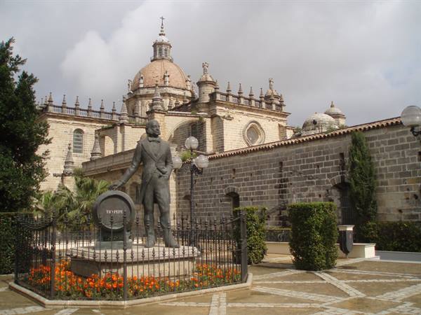 Tío Pepe statue in front of Jerez cathedral, flowerbed below cloudy sky