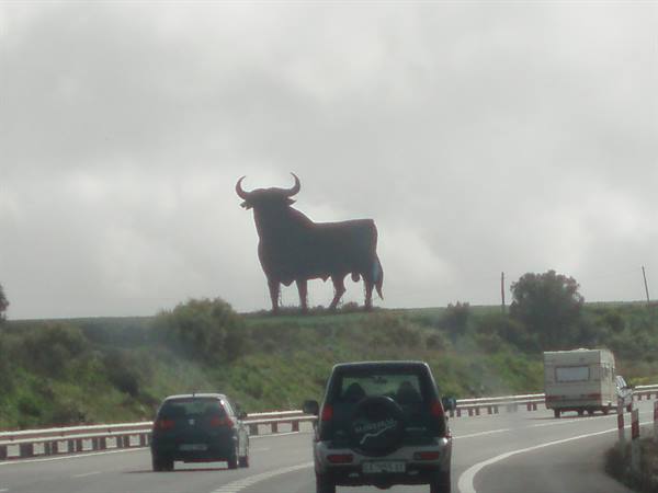Black Osborne bull billboard on green hill, cars driving on highway below